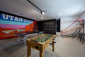 Get ready for fun in the garage game room featuring two custom murals, a ping pong table, a foosball table, pop-a-shot, and darts