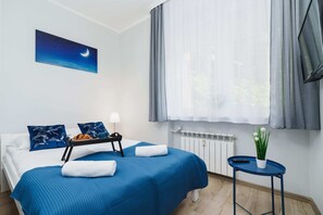 Bright, spacious bedroom with double bed with blue bedspread. A painting depicting the night sky hangs above the bed.