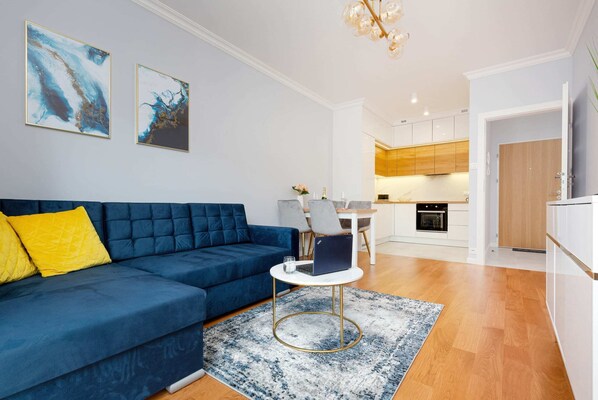 A modern living room featuring a stylish blue sofa with vibrant yellow pillows, complemented by a gray rug and a glass coffee table. Perfectly lit with natural light.