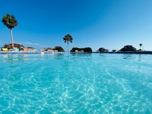 Large community pool with shaded area under the clubhouse and restrooms