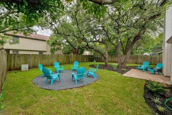 Unwind in the serene beauty of our spacious backyard, featuring several Adirondack chairs nestled under majestic oak trees. Perfect for enjoying nature and privacy in total comfort.