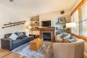 Spacious living area with flat screen TV, hardwood flooring, gas fireplace and sleeper sofa.