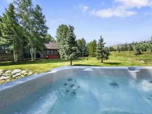 View from a hot tub looking over a grassy yard with several trees and a house in the background under a partly cloudy sky.