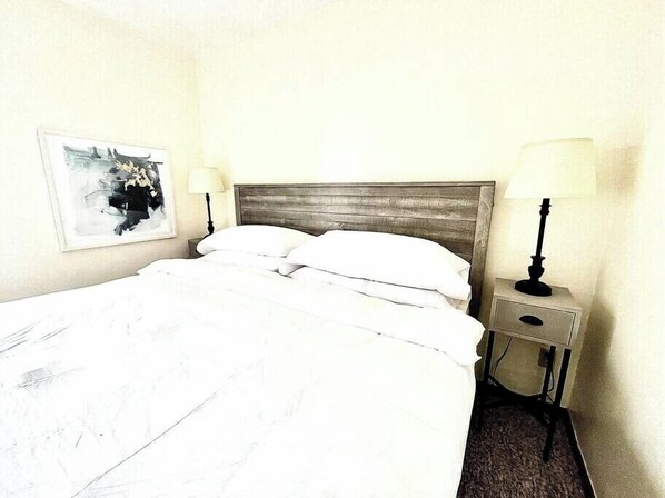 Bedroom with comfy queen matress, nightstand and bedside lamp 