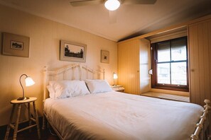 Both bedrooms feature antique wrought-iron Queen beds with plush linens that add to the cottage's historical charm