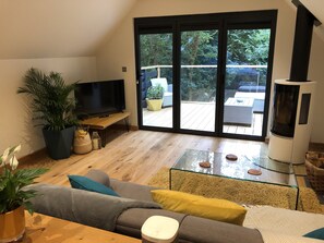 Lounge area of studio with wood burner with view to balcony and trees