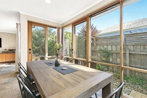 An 8-seater dining table offers space for everyone to eat together in the north-facing meals area, adjoining a light-filled, open-plan lounge & kitchen layout that opens directly to a paved courtyard & BBQ area.