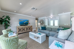 Bright & inviting living room with large L-shaped sofa, tasteful arm chairs, large Smart App TV and direct views and entrance to the amazing pool area.