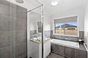 Modern bathroom with rainwater showerhead, toilet, soft towels, starter kit of toiletries, hairdryer for guests' use and a bath tub.