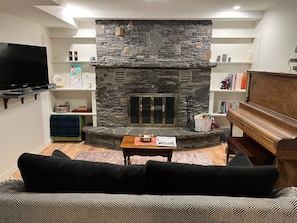 Living room with upright piano, ROKU tv and fireplace.