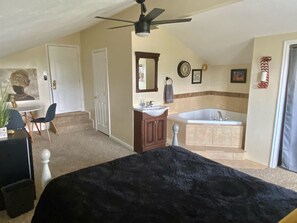 View of the Jacuzzi hot tub, queen bed, vanity, desk and door to the bathroom.