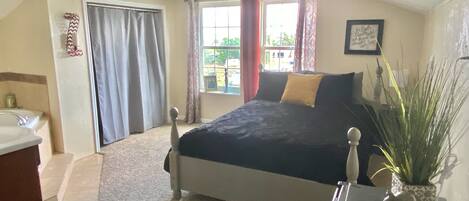 View of the queen bed and vanity from the room entrance and windows.