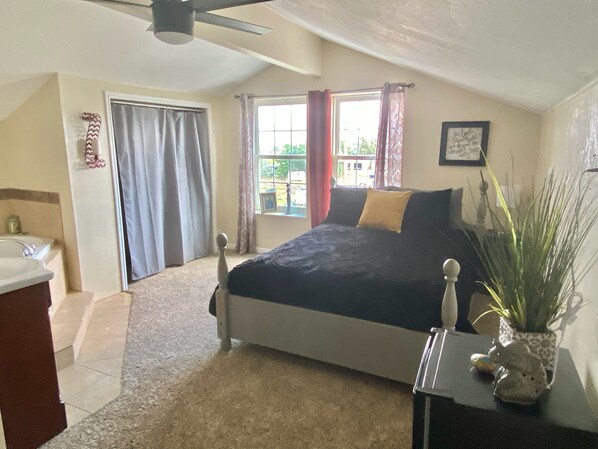 View of the queen bed and vanity from the room entrance and windows.