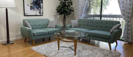 An elegant open living room with a balcony and backdrop of green spaces. 