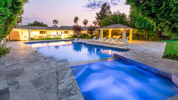 Twilight oasis: lit pool, stone patio, & elegant poolside gazebo.
