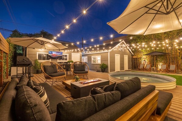 Large and lush private backyard with spacious 30 ft deck, resort lounge furniture, cantilever umbrellas, smart market lights, outdoor smart tv, firepit, and heated pool/hot tub.