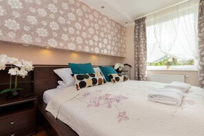 A spacious bedroom featuring floral wallpaper, a large bed with patterned bedding, and ample natural light streaming through the windows.