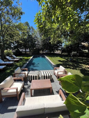 Fenced, backyard Hampton-style pool area with lounge chairs and patio