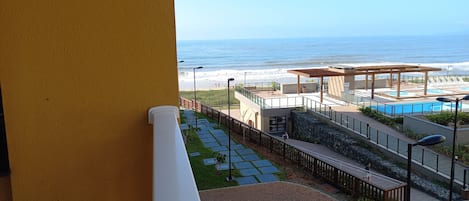 Sacada com churrasqueira, vista para piscinas e praia.