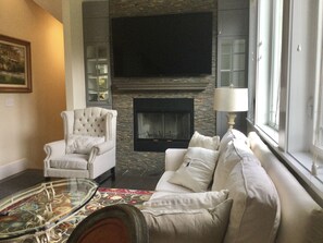 Carriage house living room with wood-burning fireplace and large TV.
