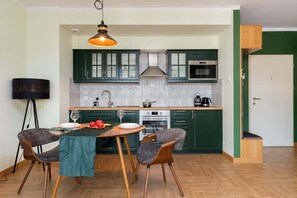 A view showing the dining area with a wooden table and chairs, next to a cozy living area with a green sofa.