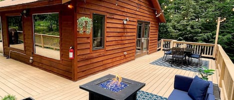 Back deck dining table & outdoor lounge couch, propane fireplace, lit by string lights. Views surrounded by the woods. Outdoor amenities Seasonal (May-Oct)