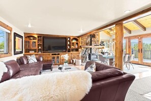 Spacious family room with luxurious sectional sofa, cozy indoor gas fireplace, tall windows, and a large flat-screen TV