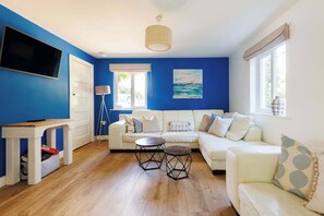 Relax in this spacious living area, featuring a comfy corner sofa, modern decor, and a large flat-screen TV, perfect for unwinding after a day of exploring the countryside.