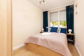 A bright bedroom featuring a comfortable double bed with pink bedding and a large window with blue curtains.