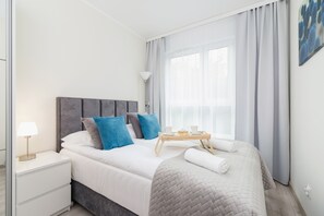 A cozy bedroom featuring a soft double bed, white furniture, and calming blue accents.
