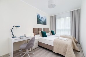 A stylish bedroom with a work desk, blue pillows, and a large window with white curtains.
