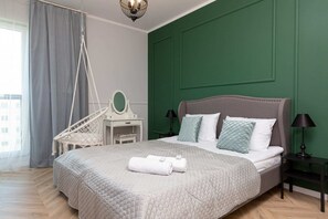 A cozy bedroom with a green accent wall, white bedding, and decorative pillows, complemented by a modern hanging chair.