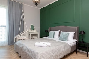 A cozy bedroom with a green accent wall, white bedding, and decorative pillows, complemented by a modern hanging chair.