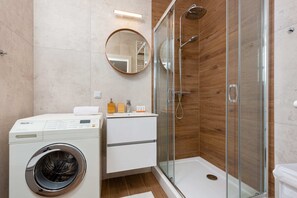 Modern bathroom equipped with a washing machine, walk-in shower, and elegant beige tiles.