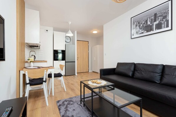 A bright and spacious living room with a sofa, coffee table, and a view of the modern, open kitchen.