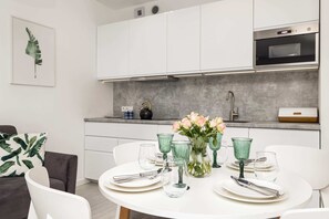 A sleek, open-plan kitchen adjacent to a dining table elegantly set with glassware and greenery.