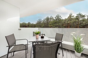 A private balcony with a compact dining setup, surrounded by lush plants and providing views of the outdoors.