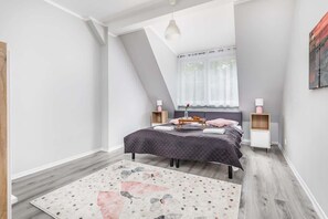 Double bed with grey bedspread in the spacious bedroom. In front of the bed, there is a carpet on the floor which gives the room a cosy feel.