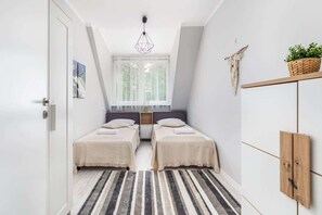 Bedroom with two single beds behind which there is a large window that lets in plenty of natural light, emphasising the unique character of the room.