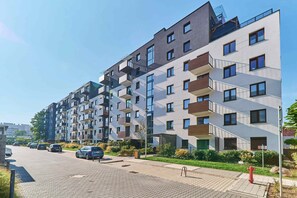 The entrance of a modern apartment complex, surrounded by greenery and well-manicured lawns, creating a welcoming first impression.