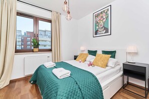 A cozy bedroom featuring a double bed with green bedding, large windows, and stylish decor accents creating a calming atmosphere.