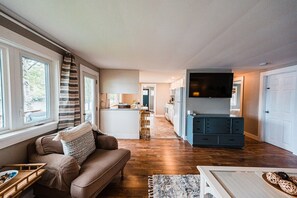 Enjoy lake views from the cozy living area, featuring comfortable seating, a large TV, and an open flow to the kitchen and dining area at Cozy Keyes Cottage.