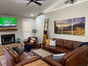 Living area includes leather couches, fireplace, vaulted ceiling and smart TV. 