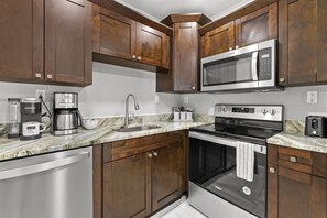 The kitchen features classic dark cabinets and stainless steel appliances, including a spacious refrigerator, oven, stovetop, and dishwasher. It’s fully stocked with all the essentials and offers both Keurig and drip coffee makers for your convenience.