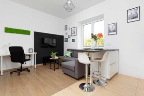 A wider view of the living room with a separate area for resting and relaxing on the grey sofa. A flat-screen TV hangs on the wall. Next to it is a desk with a chair.