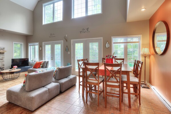 Open concept dining room and living room with large windows and high ceiling.