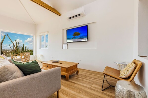 From the living room, you can enjoy the view of the outside. The living room has a TV, a comfortable sofa, and seating.