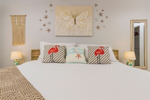 This bedroom features a king-size bed and a two-night stand with a table lamp. The wall is decorated with a wall-hung butterfly painting and macrame.