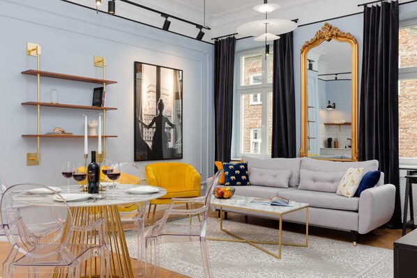 Elegant living room with a fold-out sofa bed, TV and dining area. Pastel colors with gold elements create an atmosphere of chic.