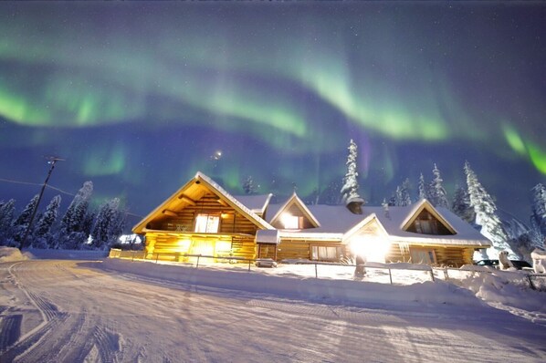 A beautiful cabin illuminated by the Northern Lights, nestled in a serene snowy landscape for the perfect winter getaway.